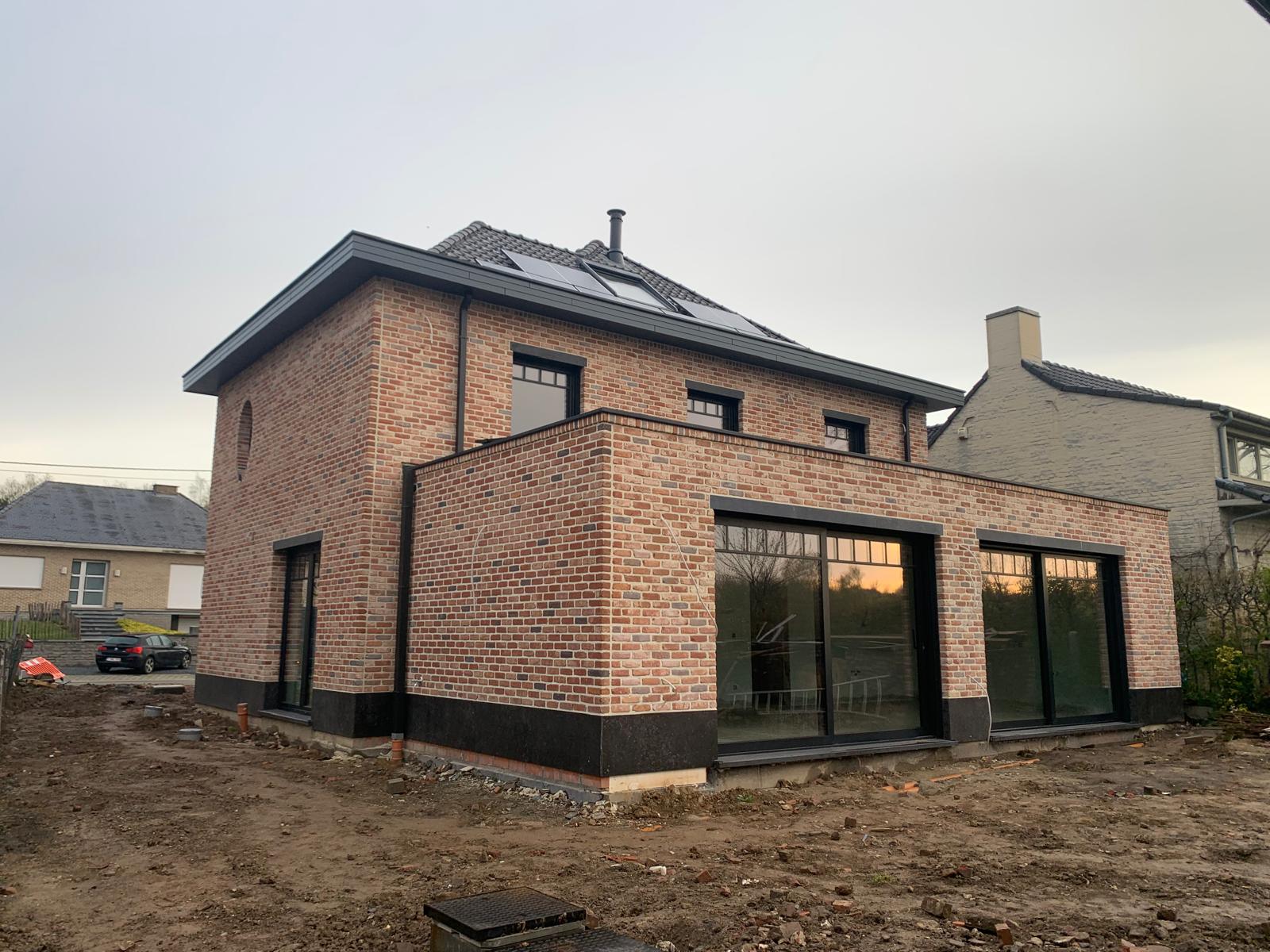 Realisatie van een strakke nieuwbouwwoning in rustiek metselwerk, voorzien van grote zwarte raampartijen.